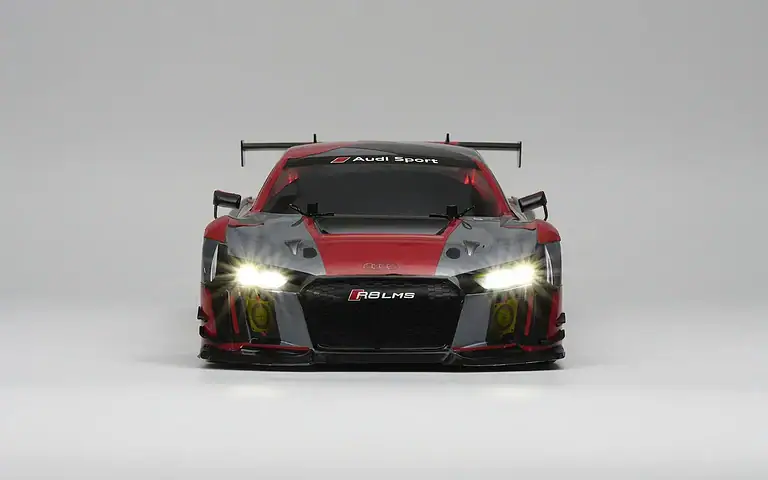 Close-up of a black and red Audi R8 LMS race car with headlights on, front view, on a plain background.