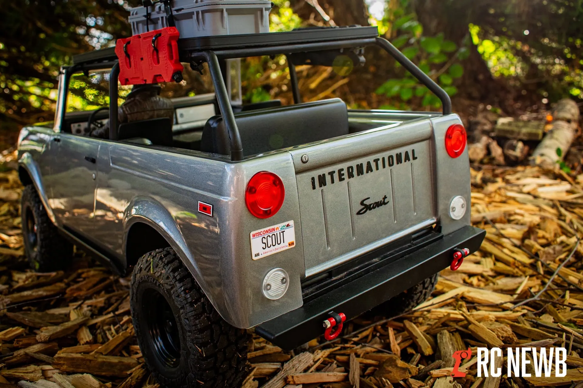 Detailed scale model of a rugged toy truck parked on fallen leaves in a wooded area, showcasing off-road tires, a detailed tailgate, and branding elements for RC Newb.