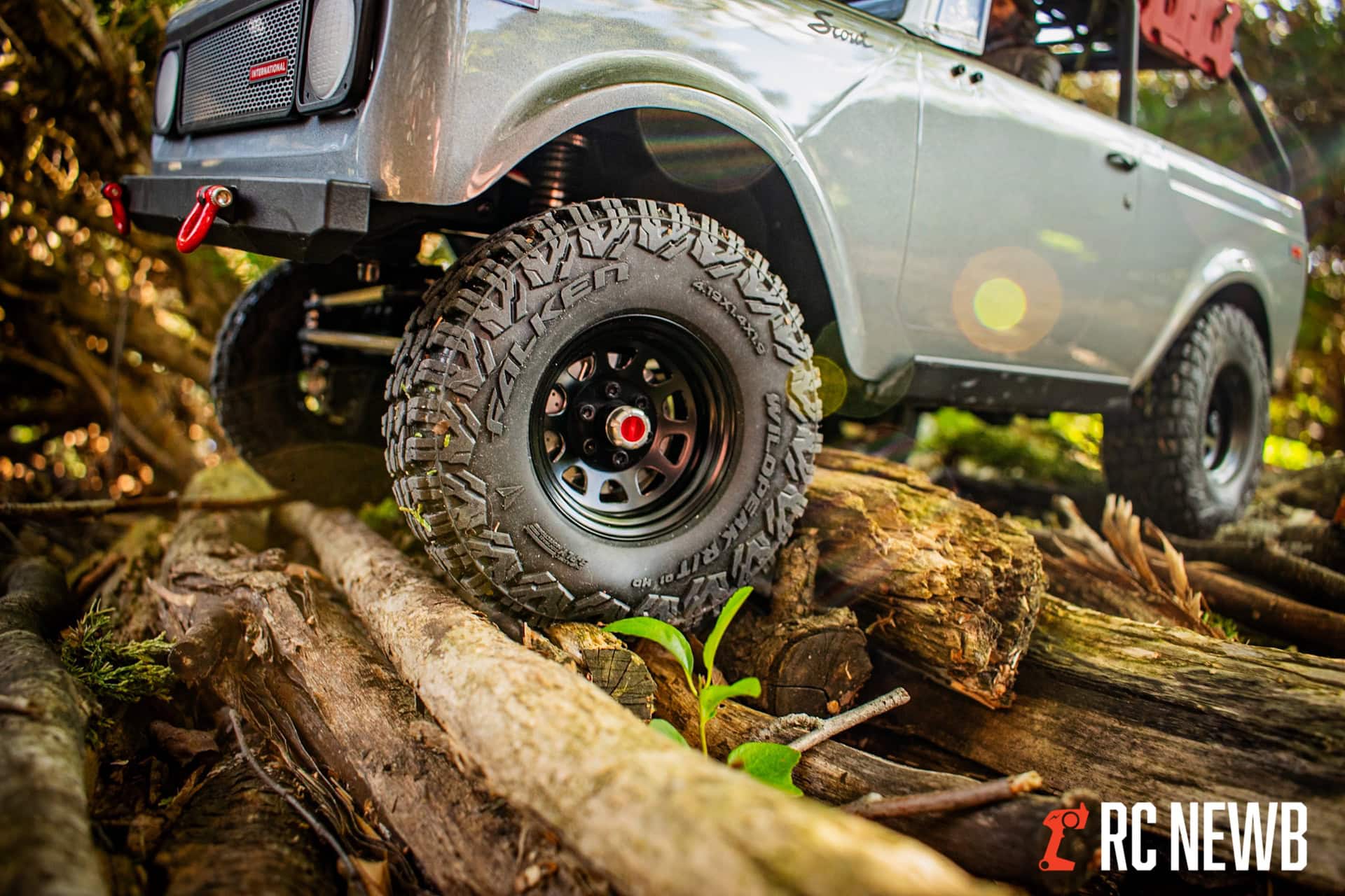 Off-road RC truck with rugged tires navigating over logs in a forest setting, demonstrating RC vehicle durability and performance on rough terrain.