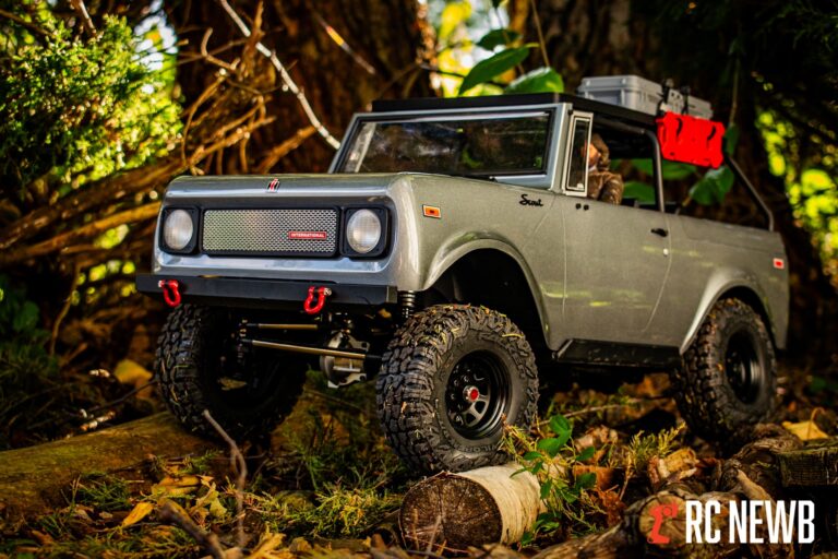 RC off-road vehicle climbing over logs in a forest setting, showcasing rugged tires and detailed design. Perfect for RC hobby enthusiasts and outdoor RC adventures.